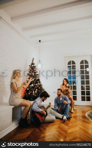 Happy young people celebrating Christmas and New Year by fir-tree at home