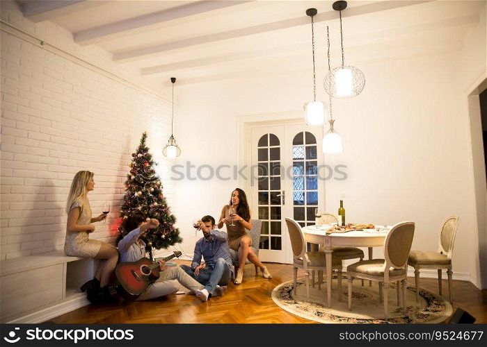 Happy young people celebrating Christmas and New Year by fir-tree at home
