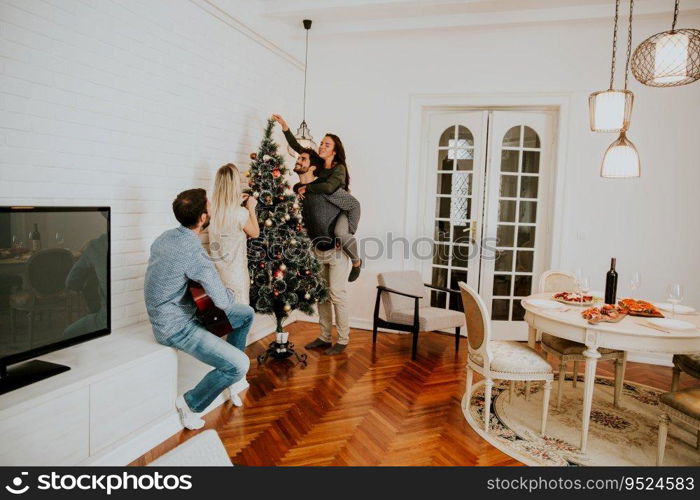 Happy young people decorate fir-tree for holidays of Christmas and New Year at home