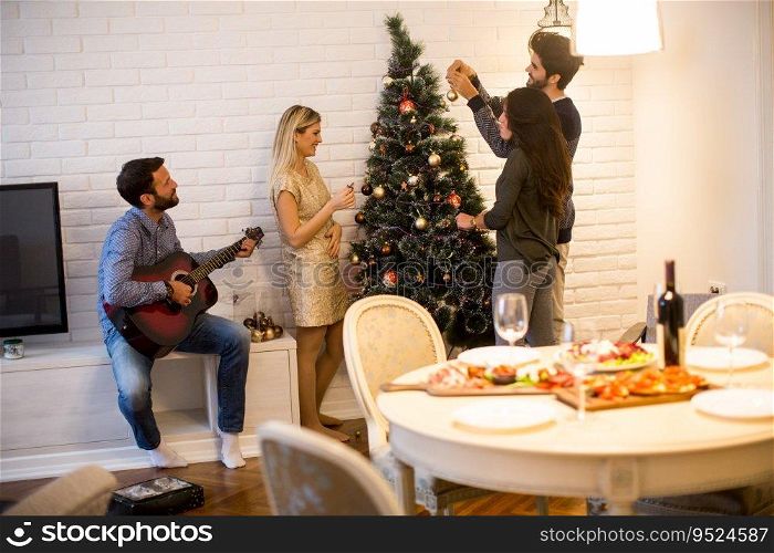 Happy young people decorate fir-tree for holidays of Christmas and New Year at home