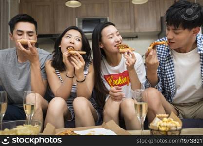 Happy young people eating pizza in the living room