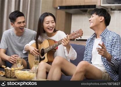 Happy young people playing guitar at home