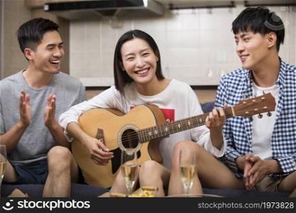 Happy young people playing guitar at home