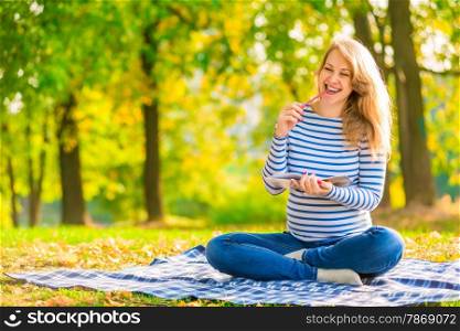 happy young pregnant girl with a notebook in a park