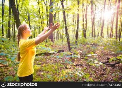Happy young pretty woman outstretching hands to sun light in forest