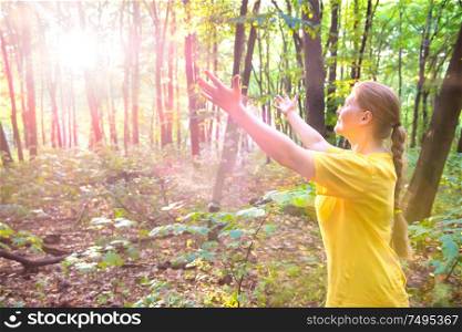 Happy young pretty woman outstretching hands to sun light in forest