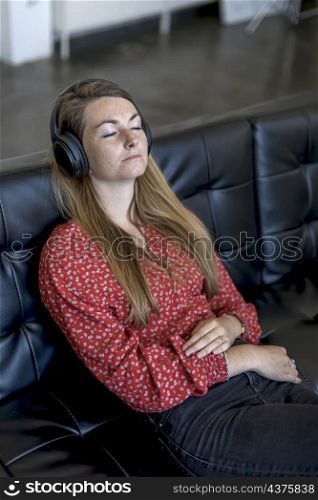 Happy young relaxed woman with headphones sitting on couch and listening to meditation music at leisure