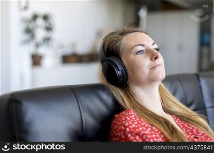 Happy young relaxed woman with headphones sitting on couch and listening to meditation music at leisure