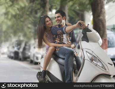 Happy young romantic couple sitting on a scooter holding hands.