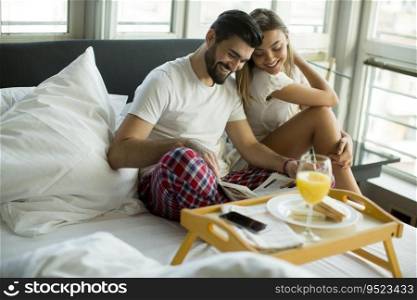 Happy young smiling couple having romantic breakfast in bed in the morning