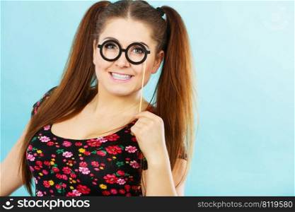 Happy young teenage woman holding fake eyeglasses on stick having fun. Photo and carnival funny accessories concept.. Happy teenage woman holding fake eyeglasses on stick