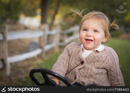 Happy Young Toddler Laughing and Playing on Toy Tractor Outside.