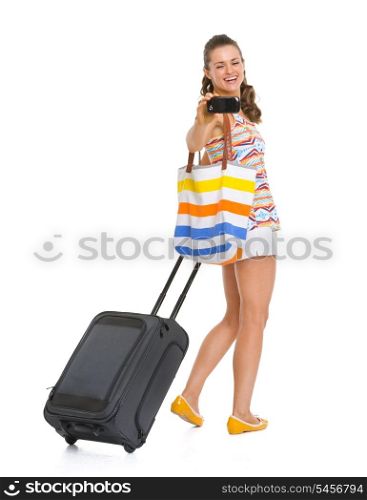 Happy young tourist woman with wheel bag taking photos with cell phone