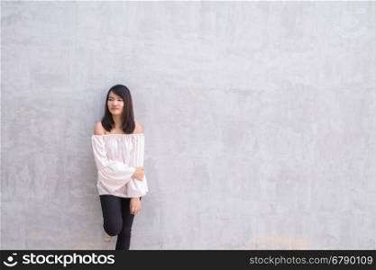 Happy young woman against concrete wall.