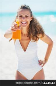 Happy young woman aiming bottle of sun block creme in camera