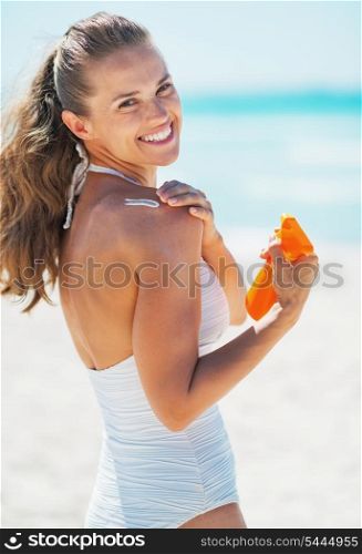 Happy young woman applying sun block creme on beach