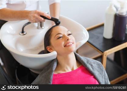happy young woman at hair salon. beauty and people concept - happy young woman with hairdresser washing head at hair salon