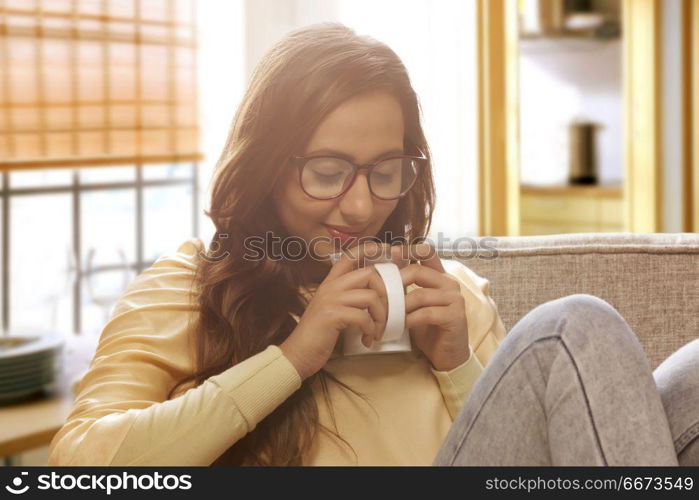 Happy young woman at home drinking cup of coffee