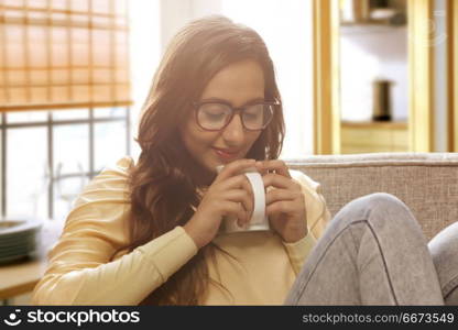 Happy young woman at home drinking cup of coffee