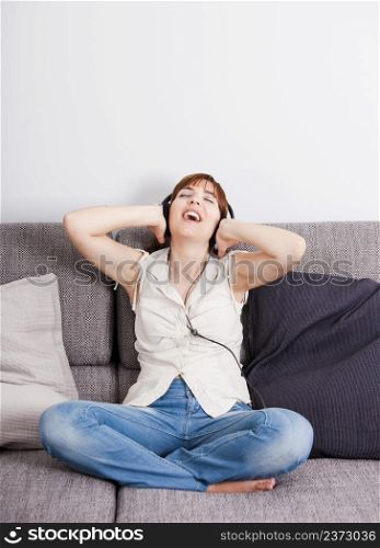 Happy young woman at home listening music with headphones