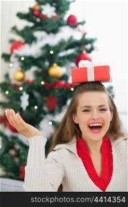 Happy young woman balancing Christmas present box on head