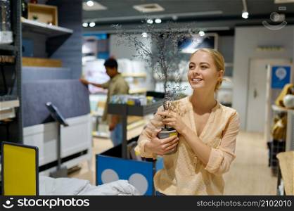 Happy young woman choosing decorative tree for home interior in furniture store shopping centre. Woman choosing decorative tree for home interior