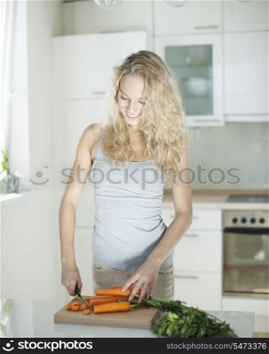 Happy young woman chopping carrots on board in kitchen