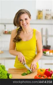 Happy young woman cutting cucumber in kitchen