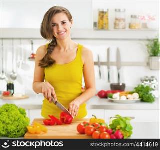 Happy young woman cutting fresh vegetable salad