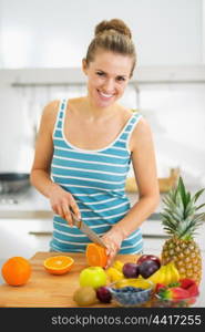 Happy young woman cutting orange in modern kitchen