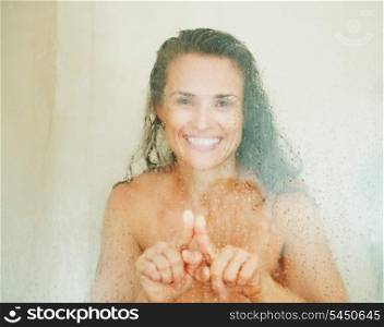 Happy young woman drawing heart in weeping glass shower door