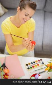Happy young woman drawing on Easter red egg
