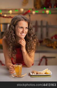 Happy young woman drinking ginger tea in christmas decorated kitchen
