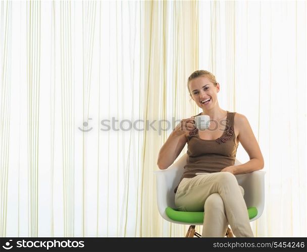 Happy young woman drinking tea in modern chair
