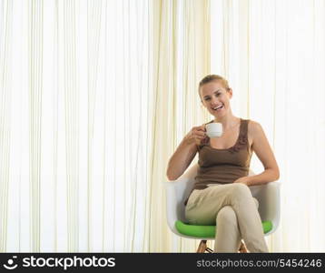 Happy young woman drinking tea in modern chair