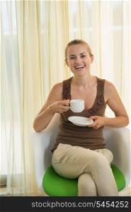 Happy young woman drinking tea in modern chair