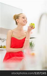 Happy young woman eating apple in kitchen