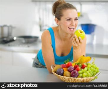 Happy young woman eating apple in modern kitchen