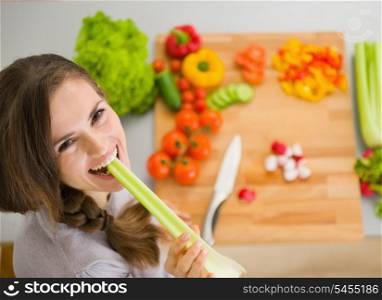 Happy young woman eating celery in modern kitchen