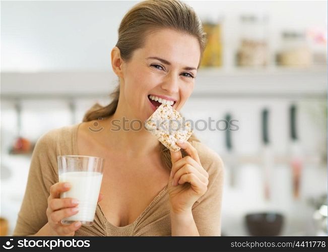 Happy young woman eating crisp bread with milk in kitchen
