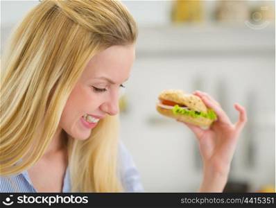 Happy young woman eating sandwich in kitchen