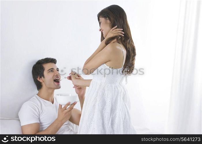 Happy young woman feeding man in bedroom