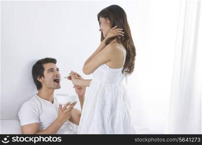 Happy young woman feeding man in bedroom