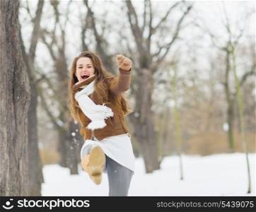 Happy young woman hitting snow with leg