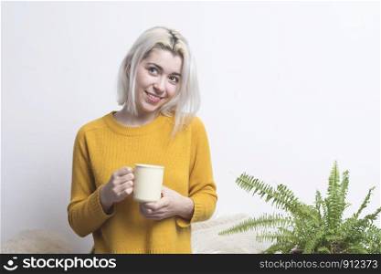 Happy young woman holding a cup of tea or coffee looking at the camera with a beaming warm smile