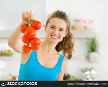 Happy young woman holding bunch of tomato in kitchen
