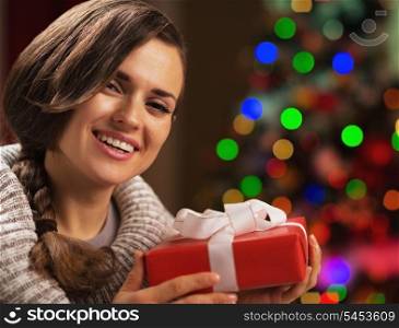 Happy young woman holding christmas present box in front of christmas lights