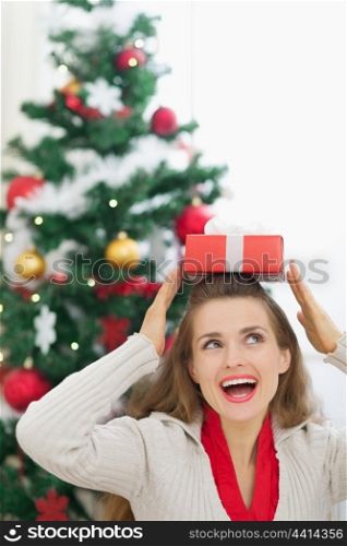 Happy young woman holding Christmas present box on head