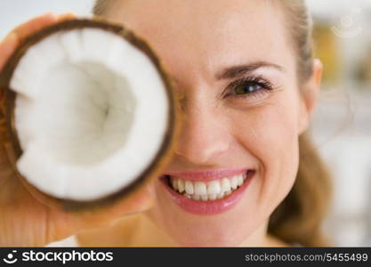 Happy young woman holding coconut piece in front of eye