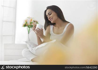 Happy young woman holding coffee cup in bedroom